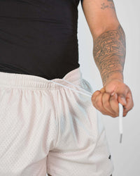 Close-up of a person adjusting the cord of 3-inch mesh shorts with an elastic waistband for a secure fit.